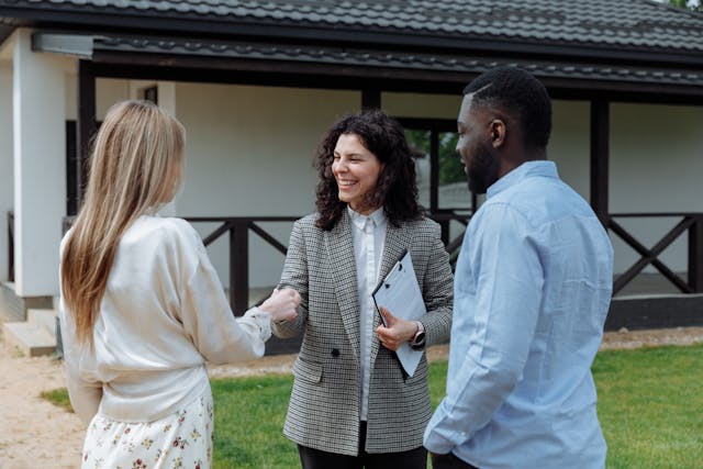 Two people shaking hands outside while another person stands near them