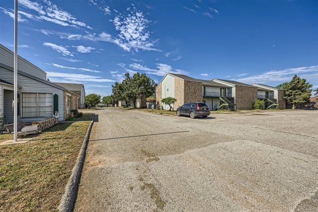 Apartment building exteriors with a paved parking lot and green spaces.