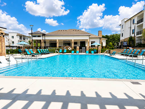 A large swimming pool with sun loungers and a building in the background.