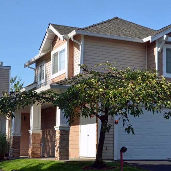 A house with a white garage door and a tree in front.