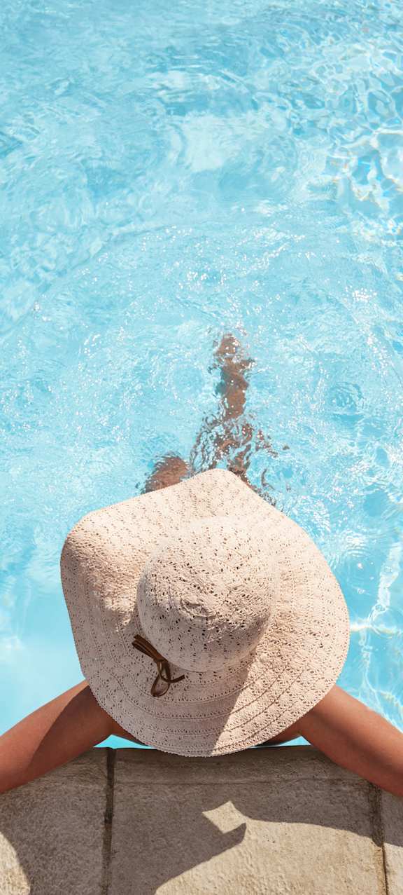 A woman in a white hat is relaxing by the pool.