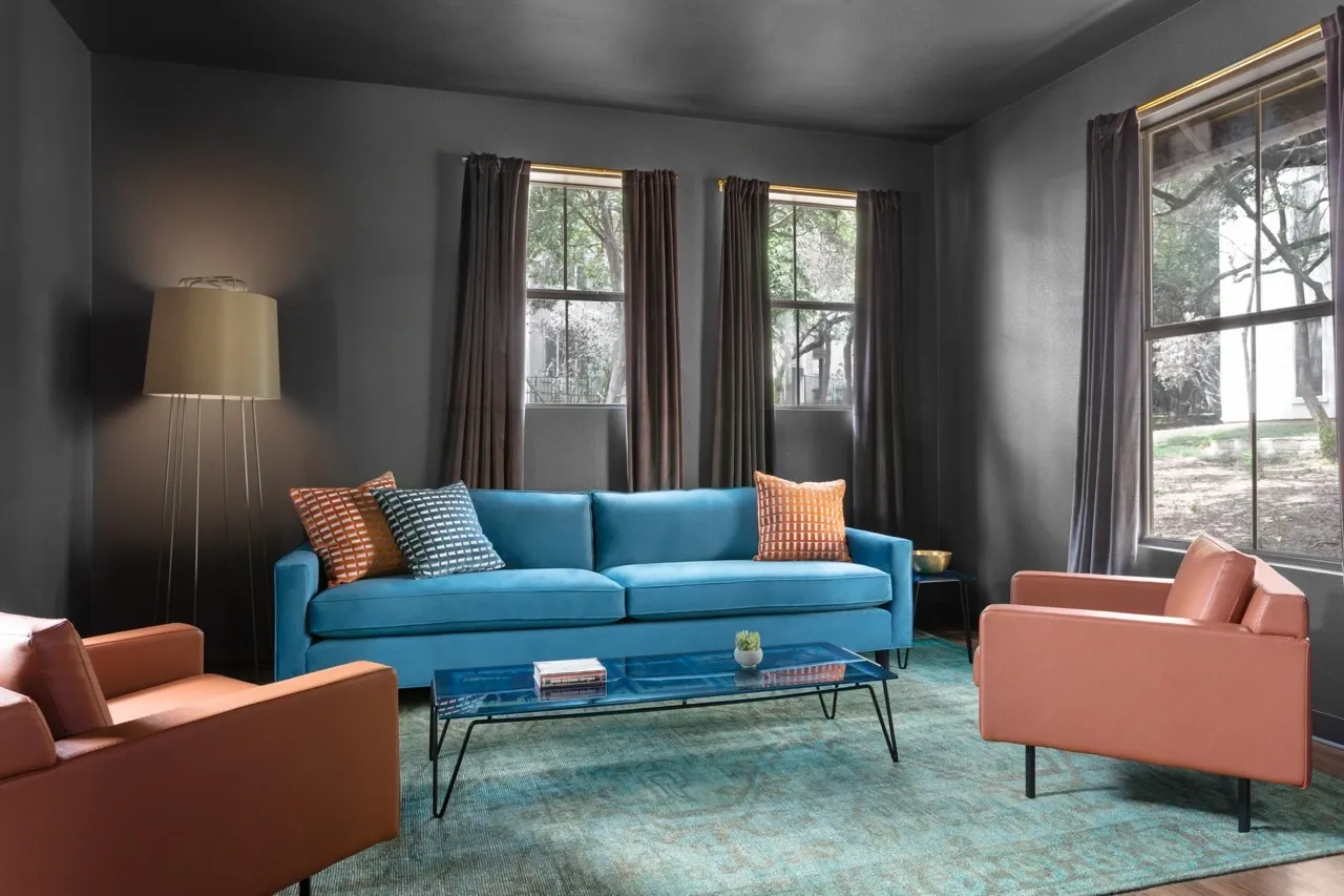 Modern living room with a teal sofa, burnt orange armchairs, and a glass coffee table.