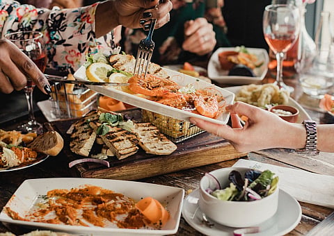 Vibrant dining table scene with delicious seafood platter, fresh grilled bread, a colorful salad, and a variety of mouthwatering dishes, creating a warm and inviting atmosphere.