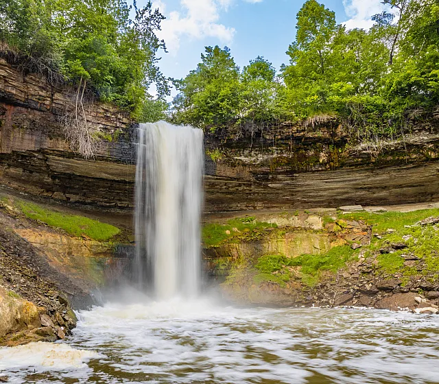 Minnehaha Regional Park majestic waterfall cascading down a rocky cliff surrounded by lush greenery, evoking a sense of tranquility and natural beauty.