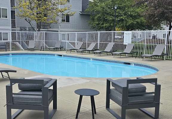 A pool surrounded by chairs and a fence.
