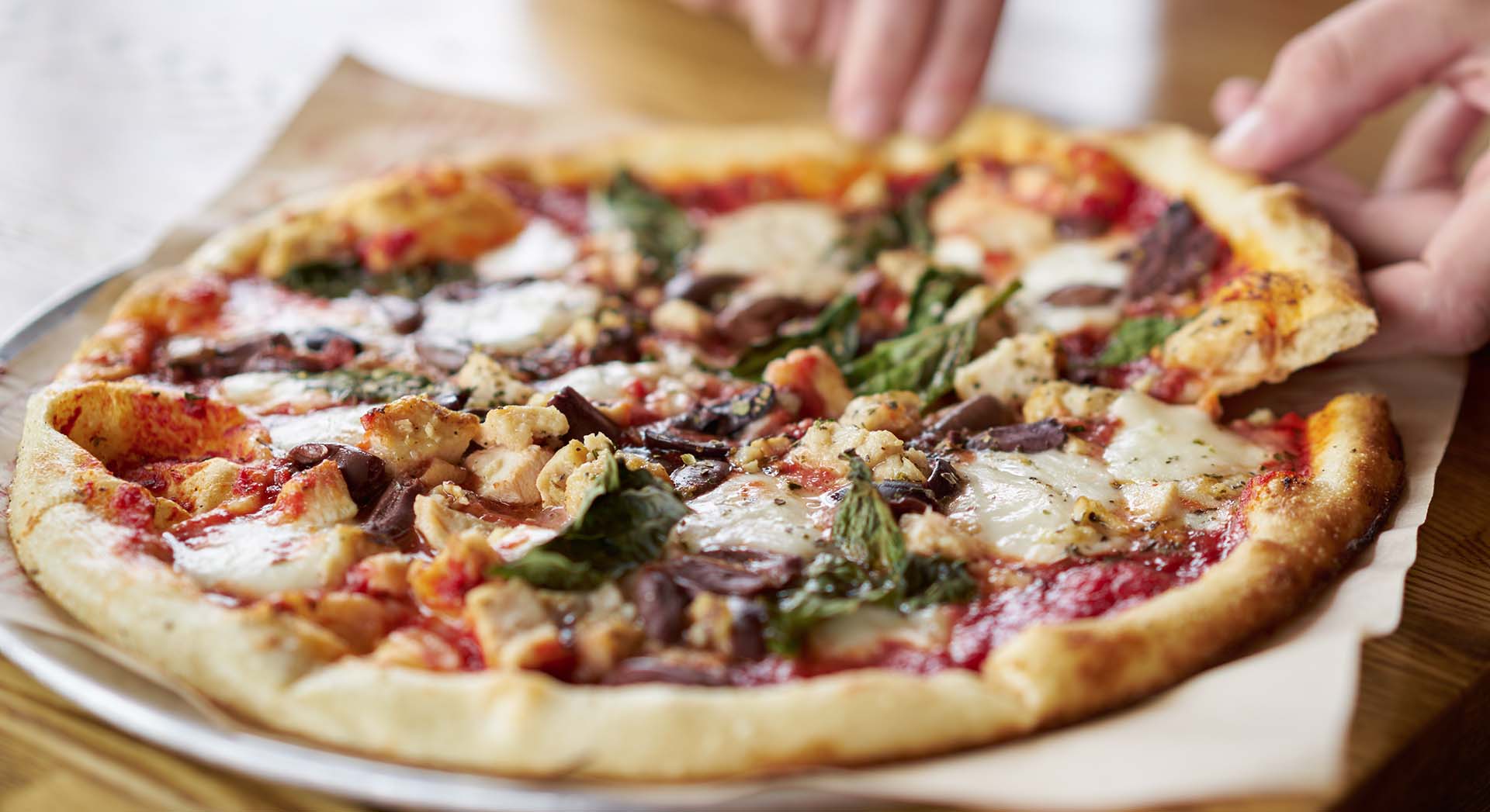 Hand removing a slice from a fresh pie of pizza margherita
