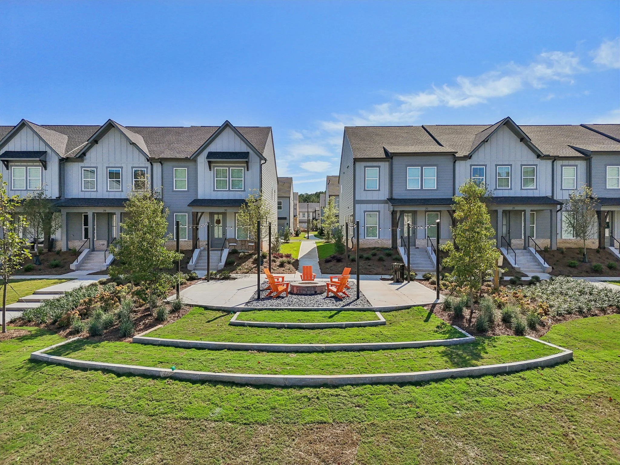 Row of gray townhomes facing a common green space with an orange Adirondack chair seating area and fire pit.