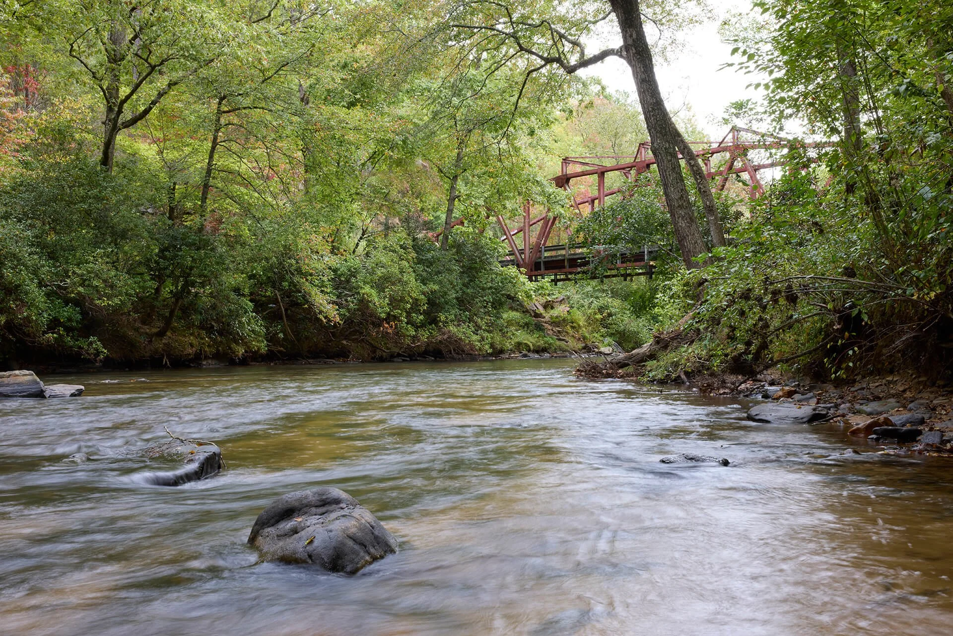 photo of shallow creek with red rusty bridge in the background