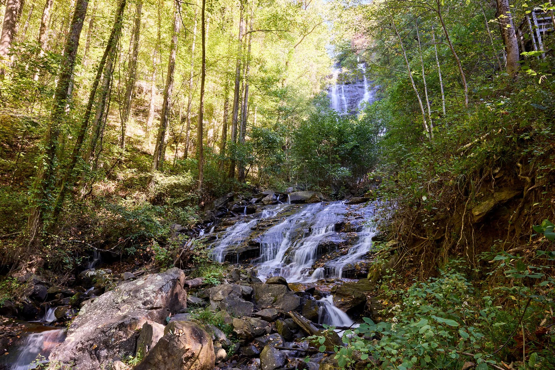 photo of tiered waterfall in forest with sun shining from top left corner