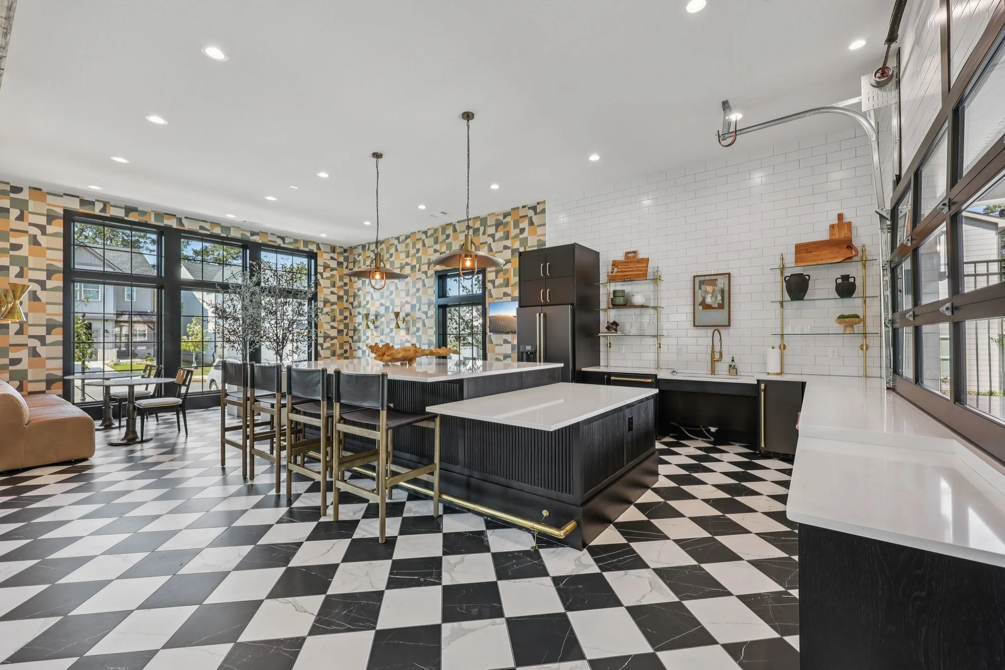 Cool clubhouse kitchen with black-and-white checkered floors, a central island with bar stools, black cabinets, and a garage-door style window.