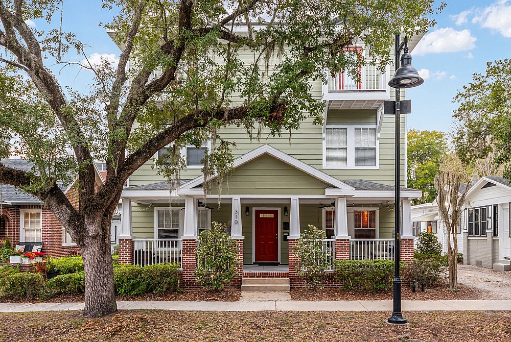 Charming two-story house with a welcoming front porch, nestled among shady trees and vibrant greenery.