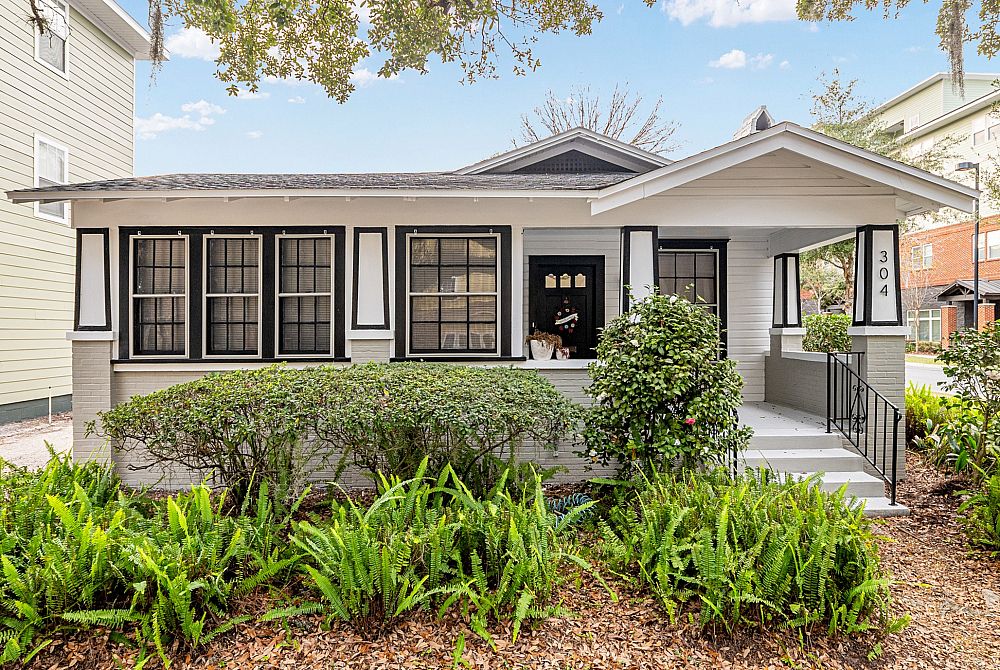 Charming bungalow with a classic front porch, vibrant greenery, and elegant vintage design.