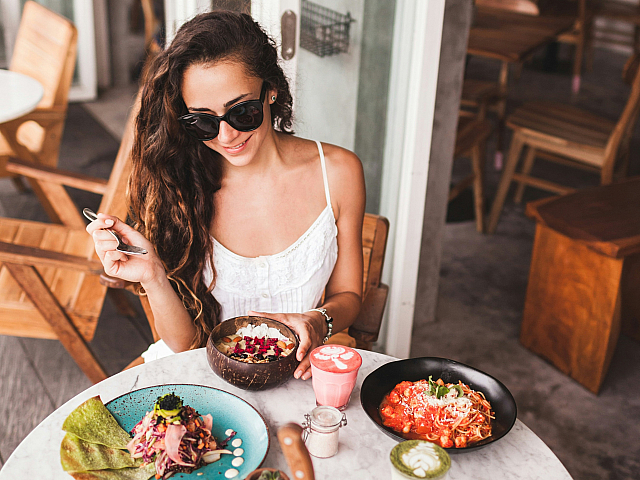 Charming cafe scene with a woman enjoying an array of colorful and delicious brunch dishes at a cozy outdoor table.