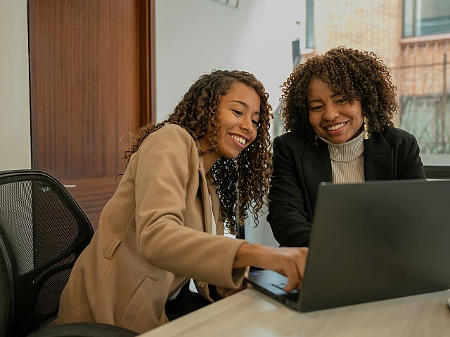 Two cheerful professionals collaborating on a laptop in a bright, modern office space.