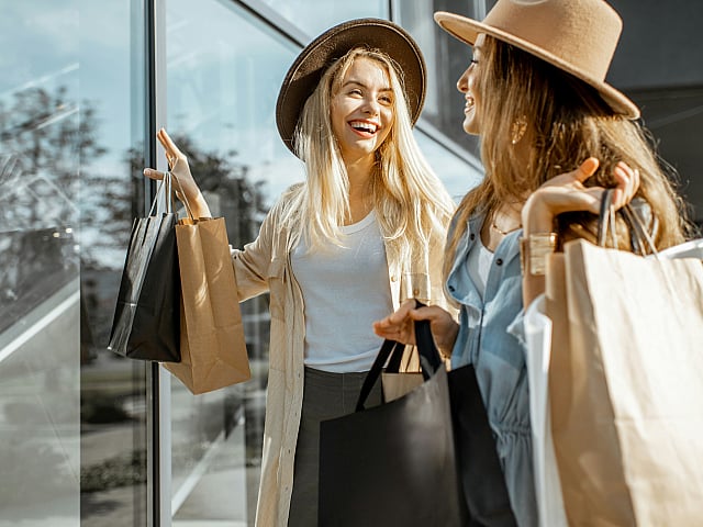 Joyful shopping experience with two stylish women in hats carrying trendy bags outside chic storefront.