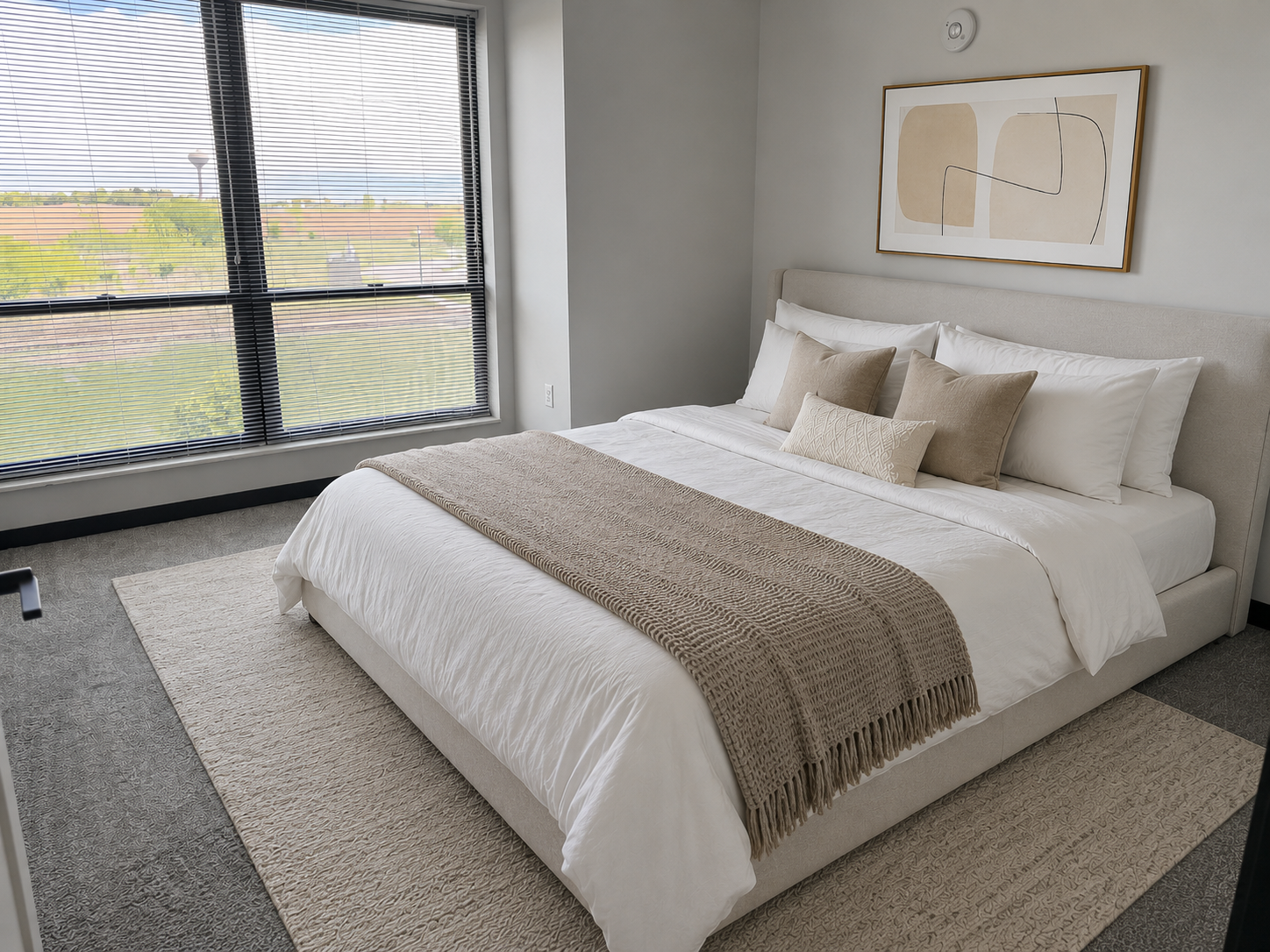 Modern bedroom with a neatly made bed, large window, and neutral decor