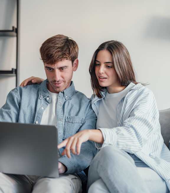 A man and woman sitting on a couch looking at a laptop. at Viridian Apartments LLC Apartments, Bowling Green