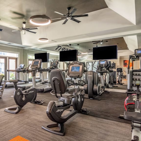 a large fitness room with cardio machines and flat screen televisions
