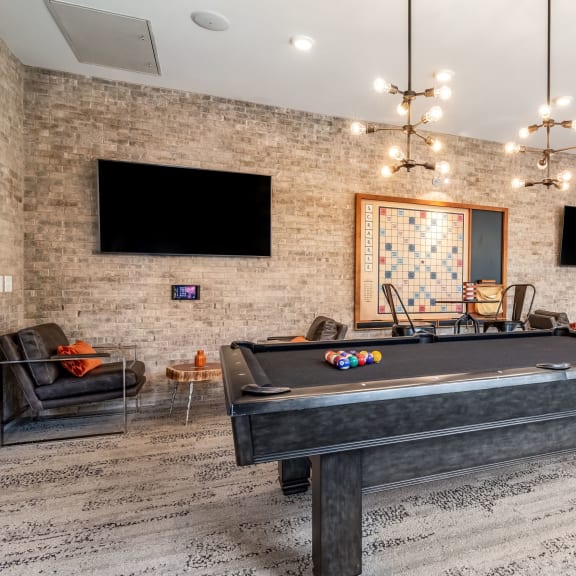 a billiards table in a clubhouse with flat screen televisions on the brick wall