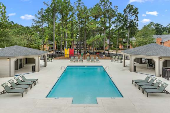 A large swimming pool surrounded by lounge chairs and trees.