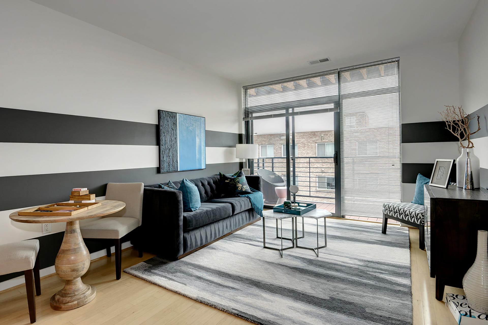 Angled view of model unit living room with dining table, sofa and coffee table, and dresser with balcony door in center of image