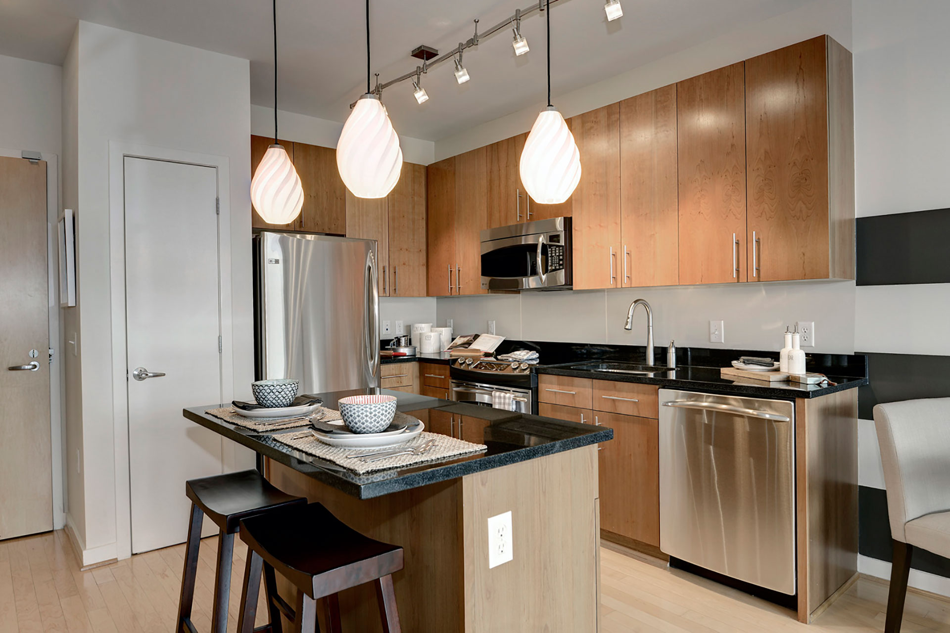 Angled view of model unit kitchen with stainless steel appliances, kitchen island, and pantry closet