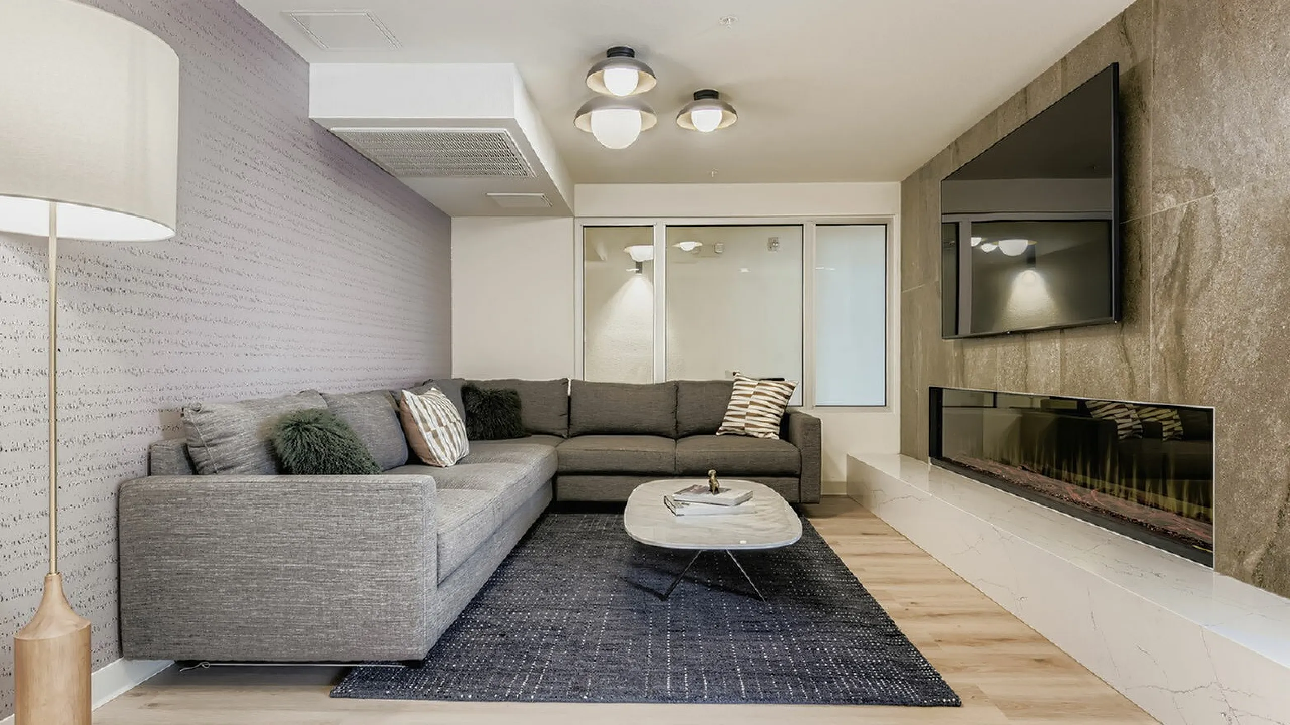Elegant living room with a cozy gray sectional sofa, chic modern lighting, and a sleek fireplace under a mounted TV.