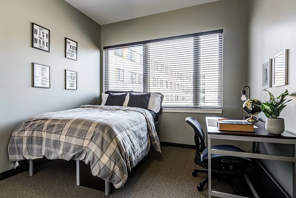 Furnished bedroom with a desk and large window at Campus West apartments for rent in Syracuse, NY.