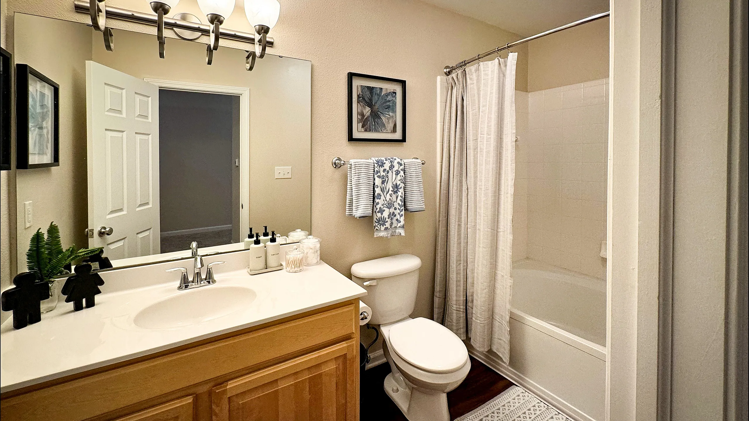 Elegant bathroom with wooden vanity, large mirror, and chic lighting. Features a bathtub with curtain, stylish decor, and vibrant plant accents.