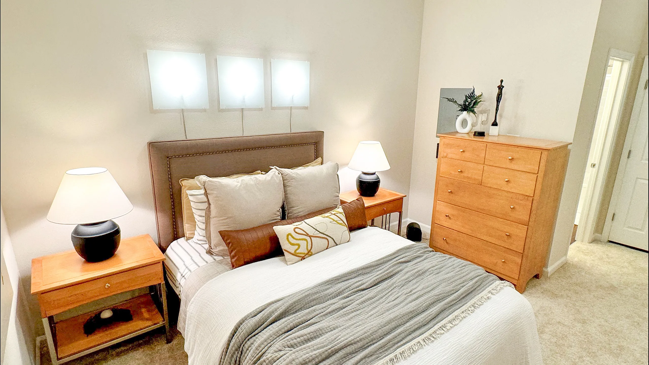 Inviting bedroom with modern decor, featuring a plush bed, elegant lighting, and a stylish wooden dresser.