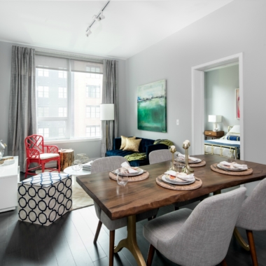 Apartment living room with 10' ceilings, large window for natural light, blue 3-seat sofa, adjacent a dining area set for four