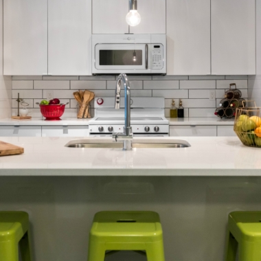 Apartment kitchen with white cabinets, white subway tile backsplash, white oven, range, microwave, island with sink with seating for three