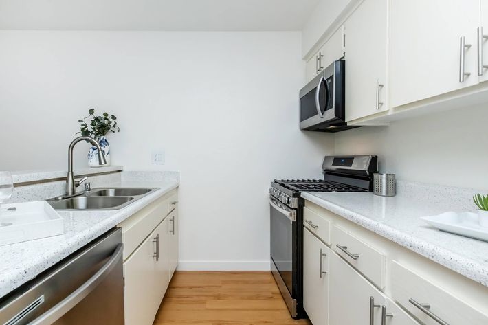 Modern kitchen featuring light-colored cabinetry, a stainless steel refrigerator, and an oven with a microwave above. The countertops are white with a subtle pattern, and there is a sink with a sleek faucet. A small plant and decorative items add a touch of style to the space.