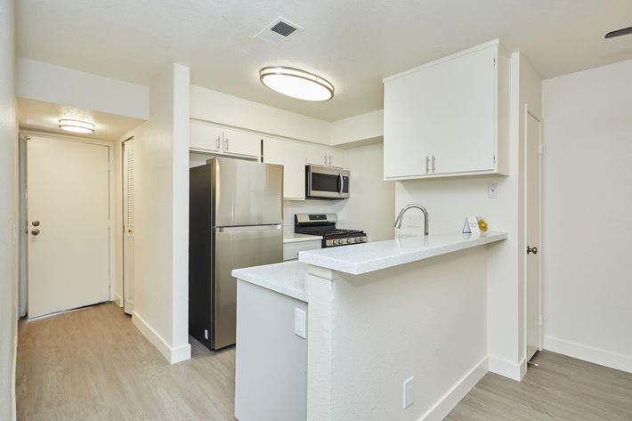 Modern kitchen featuring stainless steel appliances, including a refrigerator, microwave, and gas stove. White cabinetry and a quartz countertop provide a clean and bright look. Recessed lighting and a pendant light enhance the ambiance. The open layout connects to a living area, with light-colored flooring throughout.