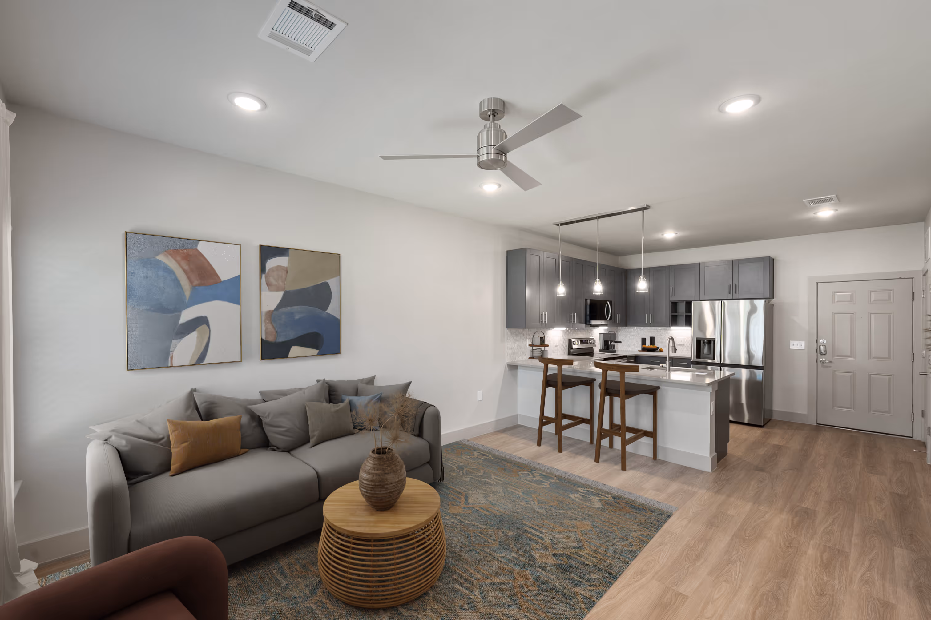 Living room with a couch and Kitchen with grey cabinets plank flooring and stainless steel appliances