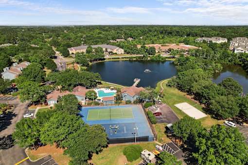 A tennis court is surrounded by trees and a lake.