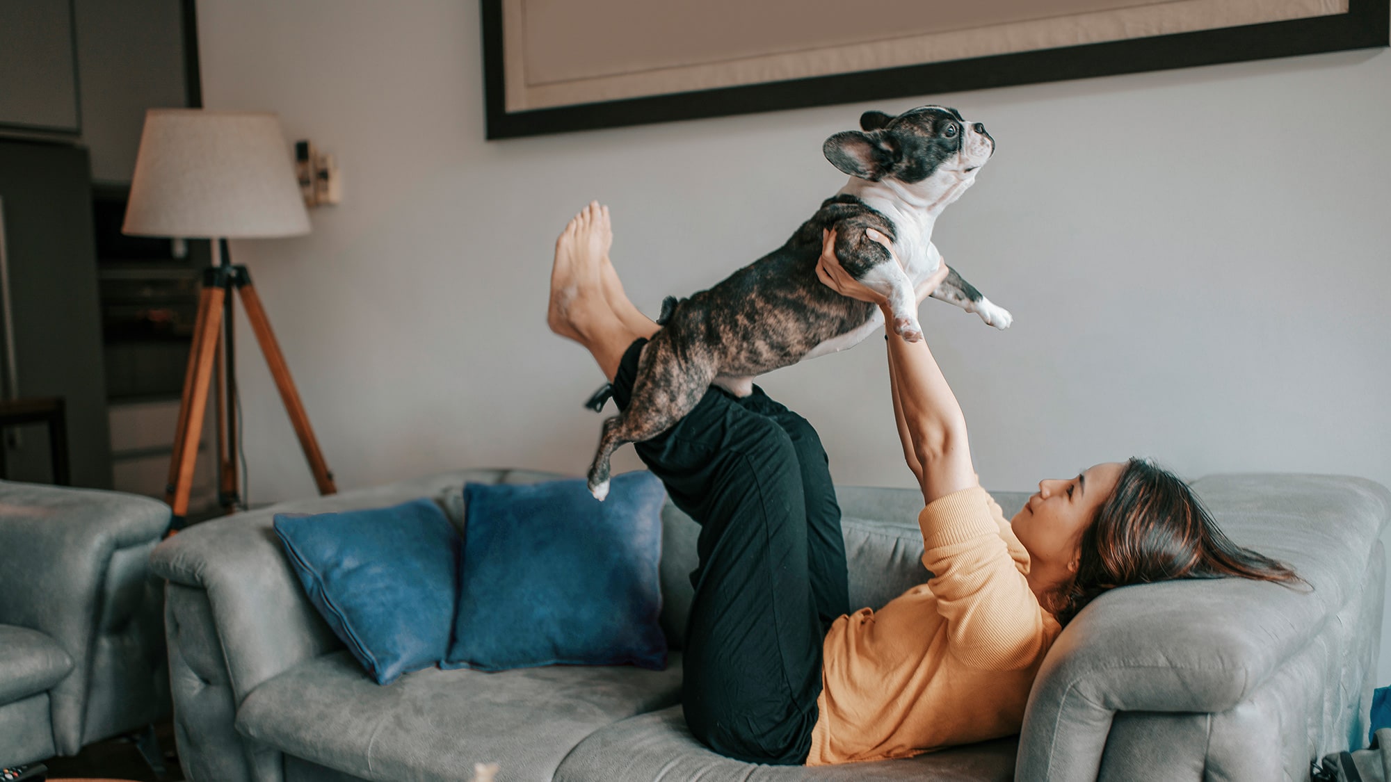 Woman lays on couch holding her dog up in the air