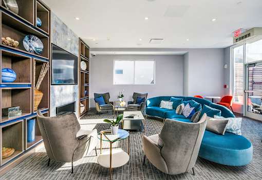 A modern living room with a grey sofa, a blue ottoman, and a glass coffee table.