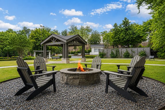 A fire pit is surrounded by four chairs in a backyard.
