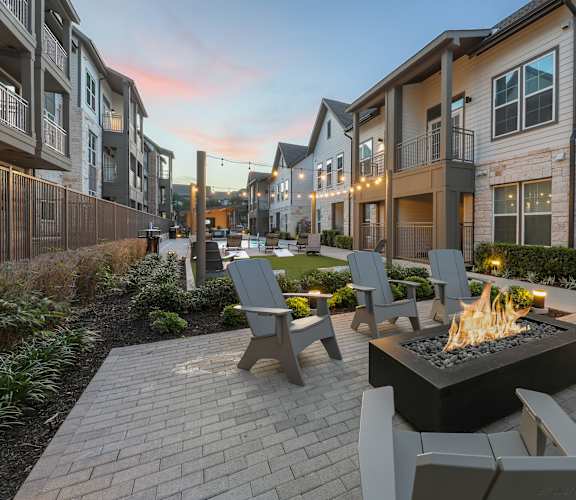 A patio with a fire pit and chairs is surrounded by apartment buildings.