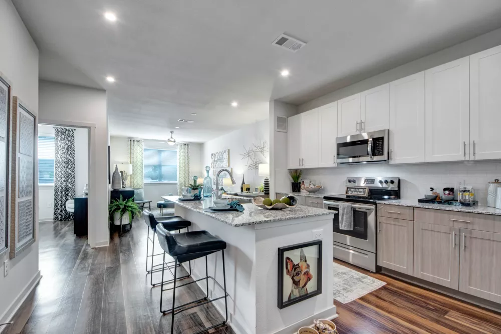 Modern kitchen at Linden Ranch Apartments featuring white cabinets, granite countertops, stainless steel appliances, and a spacious island with bar seating overlooking the open living area.