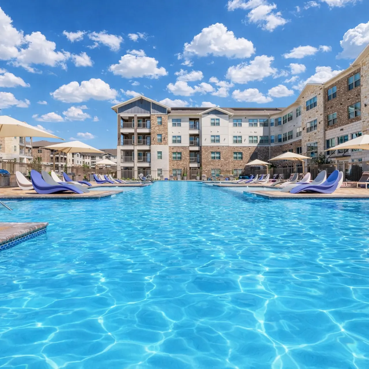 A bright blue swimming pool surrounded by modern apartment buildings and lounge chairs under umbrellas.