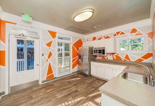 A kitchen with orange and white walls and wooden floors.