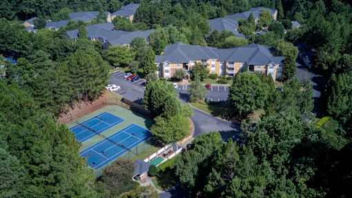 A tennis court surrounded by trees and houses.