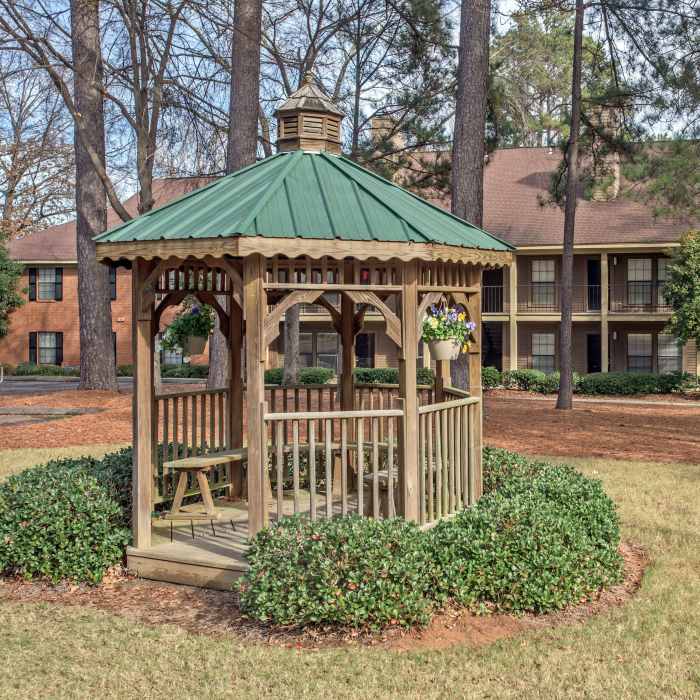 Wooden gazebo surrounded by greenery in a landscaped outdoor area with nearby apartment buildings at Stevens Creek Commons in Augusta, Georgia