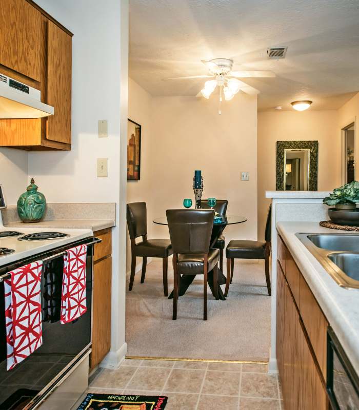 Modern kitchen with stainless steel appliances and wood-style flooring, dining area with glass table and four chairs at Stevens Creek Commons in Augusta, Georgia