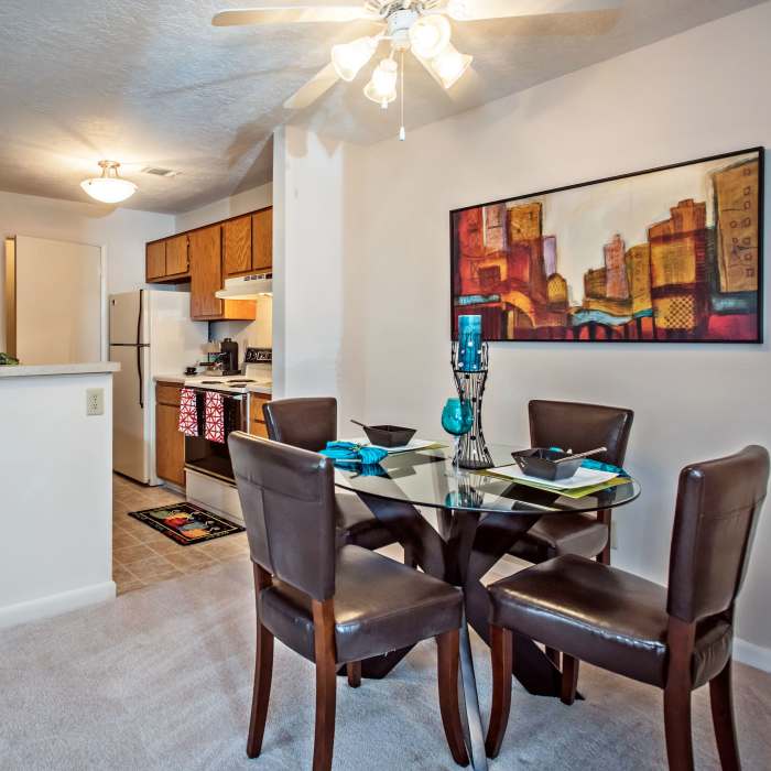 Dining area with glass table, four brown chairs, and kitchen featuring wooden cabinets and stainless steel appliances at Stevens Creek Commons in Augusta, Georgia