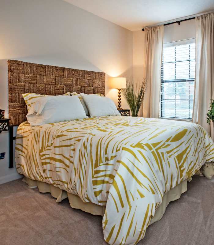 Cozy bedroom with a patterned duvet, bedside lamps, and large windows allowing natural light at Stevens Creek Commons in Augusta, Georgia