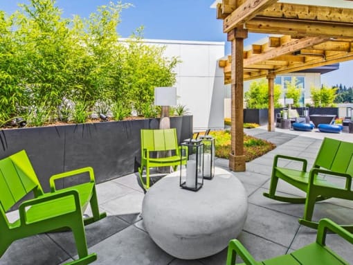 North Seattle, WA, Apartments with In-Unit Washer and Dryer - Origin - Rooftop Patio with Rocking Chairs, Stone Table, Wooden Pergola, and Plants.