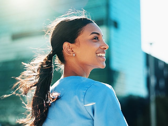 Vibrant urban scene featuring a person smiling with modern architecture and sunlight flares.